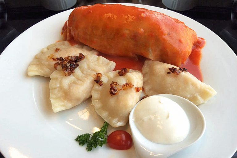 ensemble of 4 pierogi and 1 cabbage roll with sour cream on a side