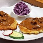 picture of beef goulash with potato pancakes and side salad
