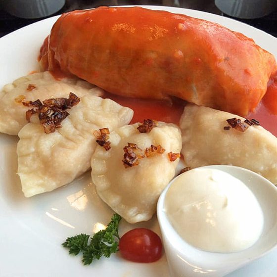 ensemble of 4 pierogi and 1 cabbage roll with sour cream on a side